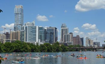 Austin skyline from a low perspective on Lady Bird Lake with people paddle boarding and kayaking in the sunshine