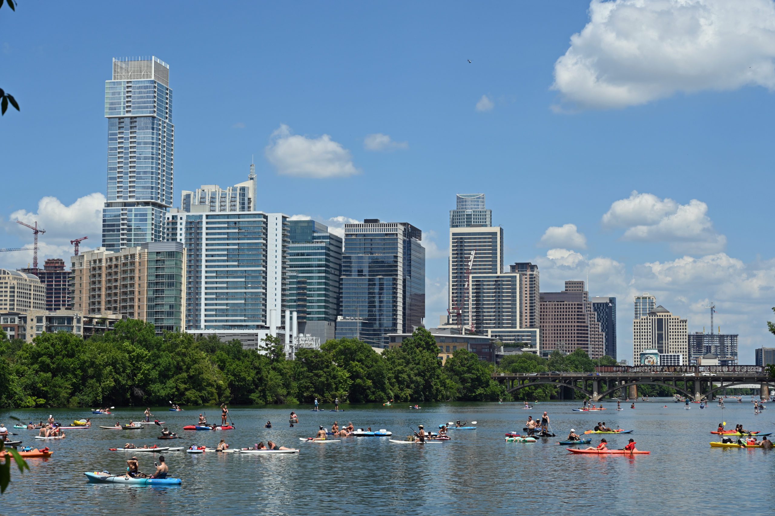 Austin skyline from a low perspective on Lady Bird Lake with people paddle boarding and kayaking in the sunshine