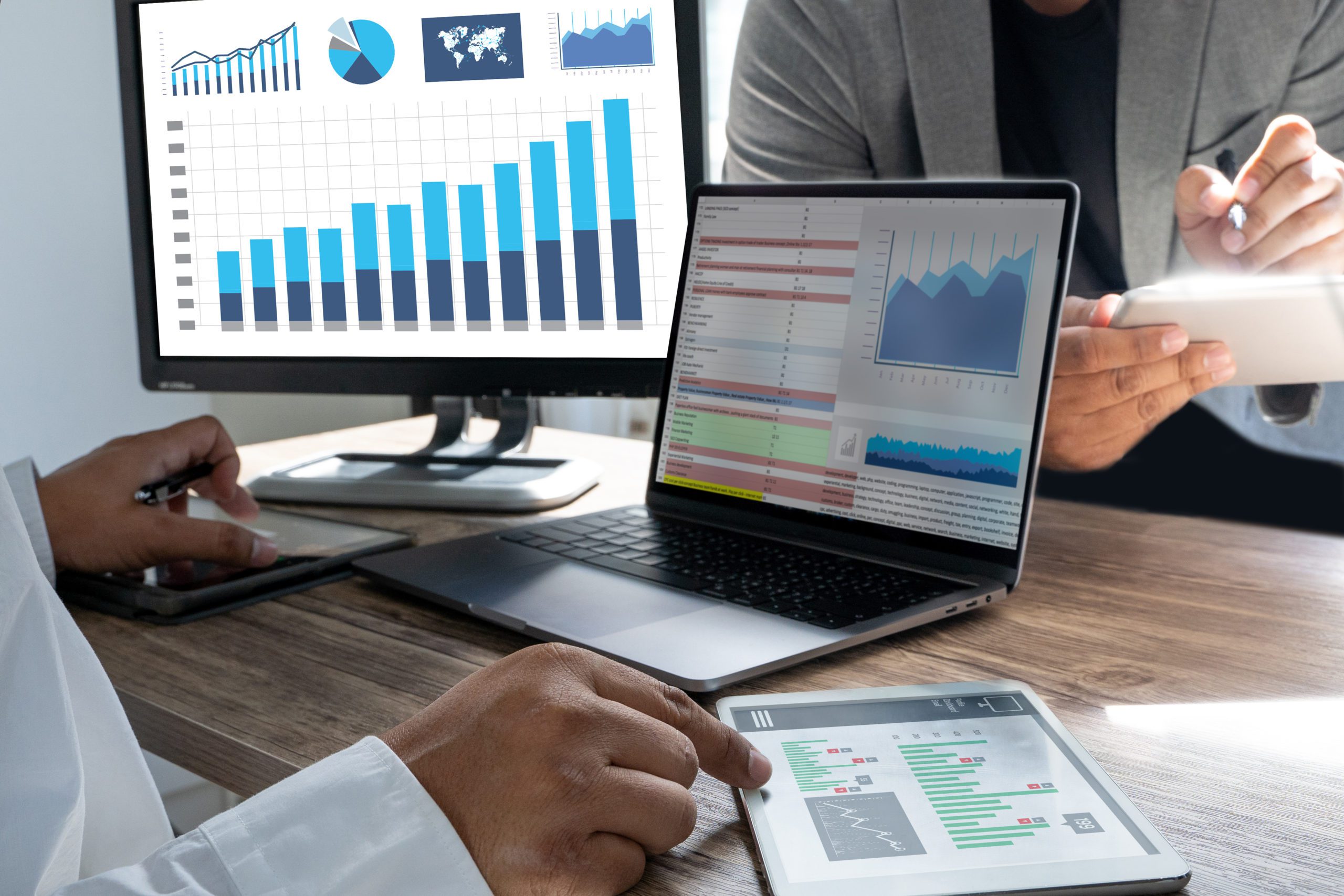 Various charts and graphs on several screens on a desk with two people's hands